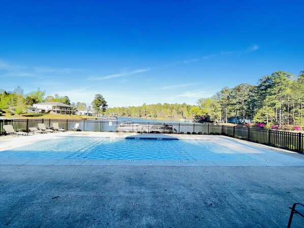 A swimming pool with a black fence, surrounded by trees and a clear blue sky.