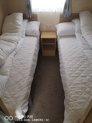 Two single beds with quilted mattresses and white pillows, a nightstand, and a window with a sheer curtain.
