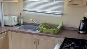 Una cocina compacta con un lavamanos, un escurreplatos verde, un tostador y una tetera.