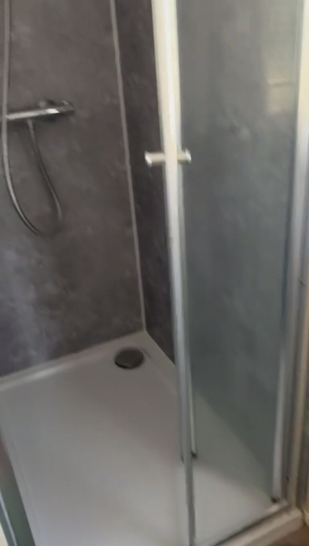 A glass-enclosed shower stall with a metal frame and a drain.