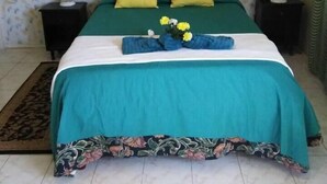 Ein Bett mit grüner Bettdecke, zwei gelben Kissen und einem blumigen Fußteil.