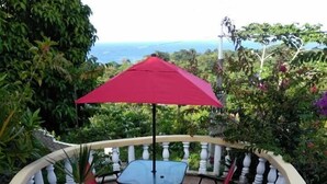 Eine Terrasse mit Tisch, Stühlen, einem roten Sonnenschirm und einem weißen Geländer.