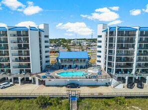 Un hotel con piscina central, varios balcones y zona de estacionamiento.