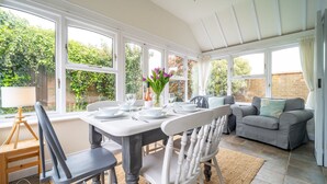 Un coin repas avec une table dressée pour quatre personnes, entouré de chaises blanches, d’un canapé et d’une lampe.
