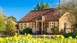 Une maison à deux étages, avec un toit en pente, des fondations en pierre et une véranda à l’avant.