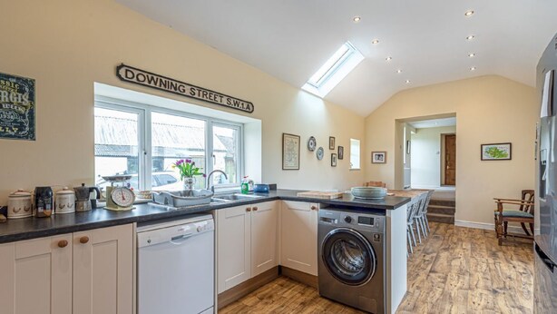 A kitchen with white cabinets, a washing machine, a sink, and a window with a view of the street. - Gwlgri -  an apartment that sleeps 8 guests  in 4 bedrooms (Holyhead)