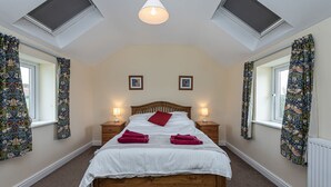 A bedroom with a wooden bed, two bedside tables with lamps, a skylight, and floral curtains. - Gwlgri -  an apartment that sleeps 8 guests  in 4 bedrooms (Holyhead)