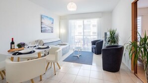 A modern living room with a dining area, a sofa, a coffee table, and a large potted plant. - L'Hippocampe T2 avec Balcon by Interhome (Les Sables d'Olonne)