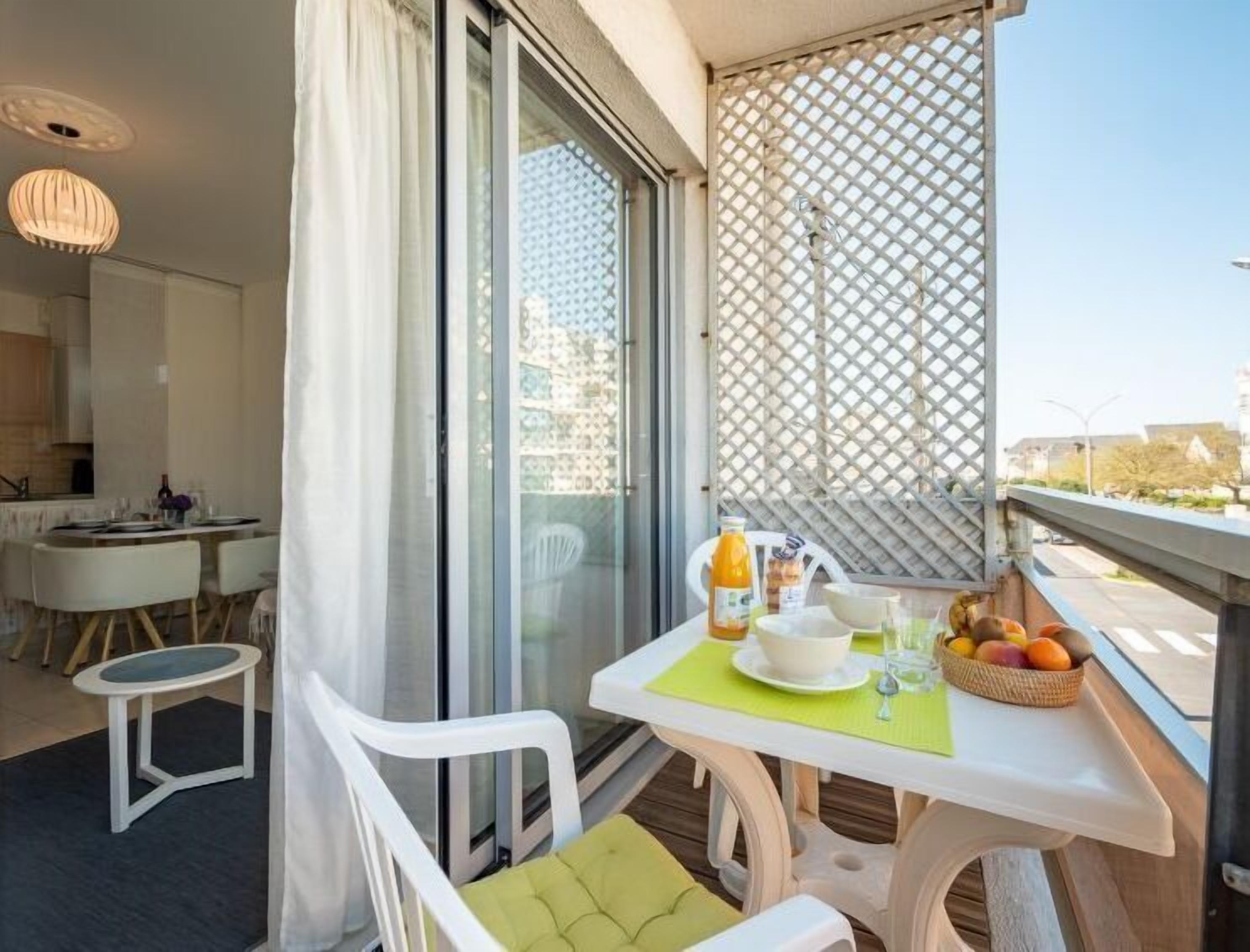 A balcony with a table set for breakfast, including a bowl, a bottle of orange juice, and a basket of fruit. - L'Hippocampe T2 avec Balcon by Interhome (Les Sables d'Olonne)