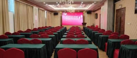 A conference room with rows of tables and chairs, a projector screen, and a chandelier.