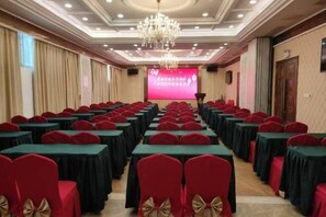 A conference room with rows of tables and chairs, a projector screen, and a chandelier. - Zhuji Hotel Nanxiong (Nanxiong)