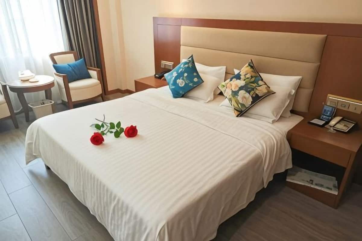 Quarto de hotel com uma cama grande, duas mesas de cabeceira, uma cadeira e uma pequena mesa.