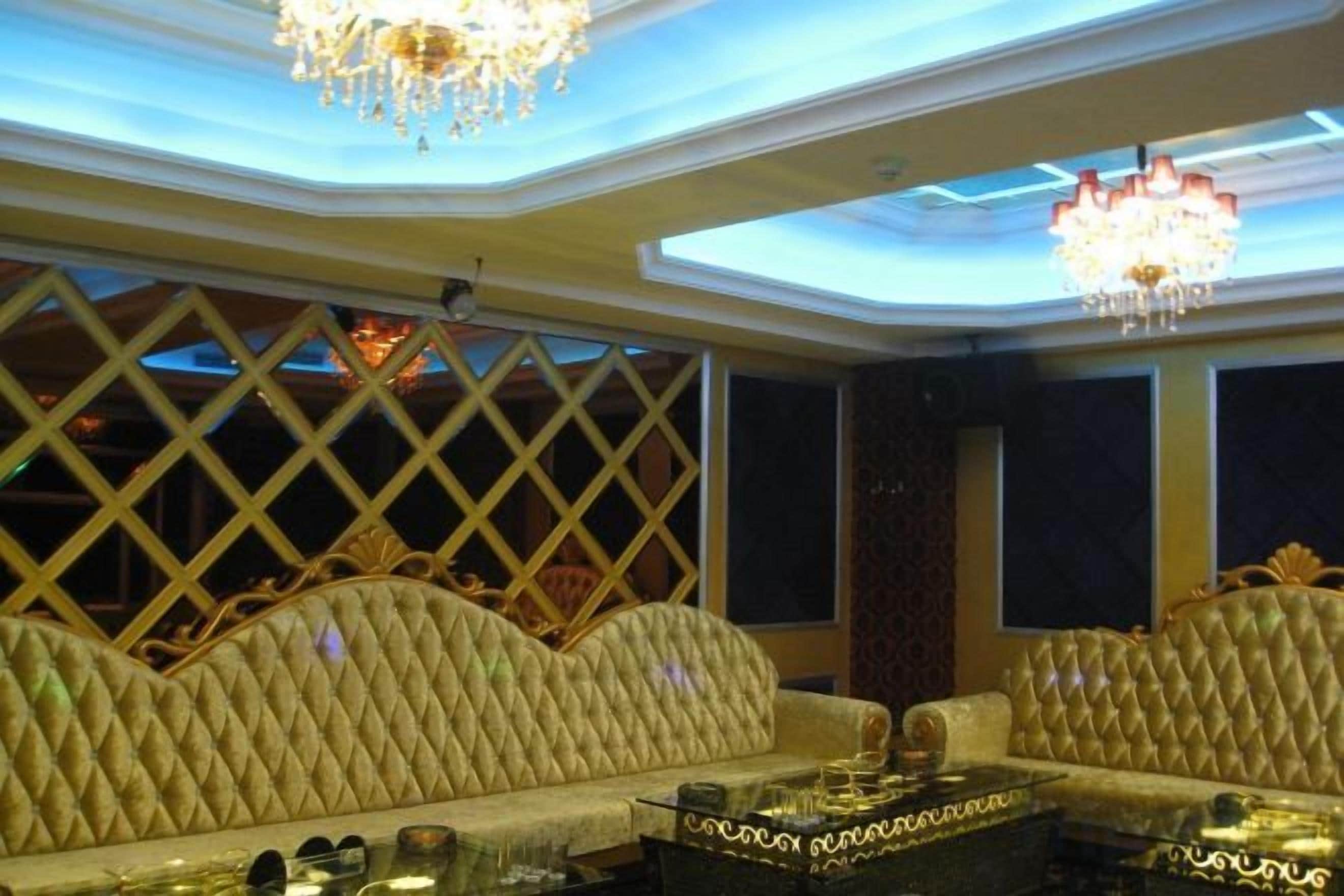 A room with a high ceiling, ornate chandeliers, and a cushioned seating area.