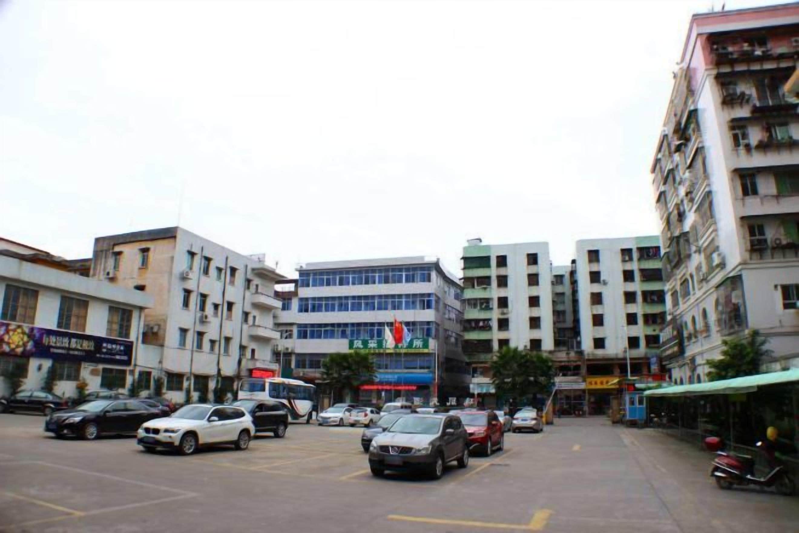 A multi-story building with a central entrance, surrounded by parked cars and other buildings.