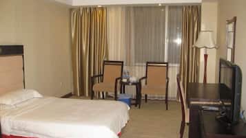 Habitación de hotel con cama, dos sillas, escritorio con televisor y ventana con cortinas.