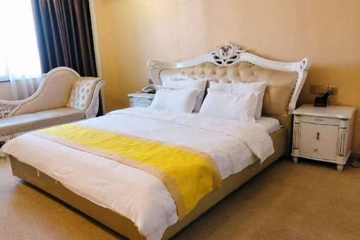 Una habitación de hotel con una cama grande, una mesita de noche, una silla y una ventana con cortinas.