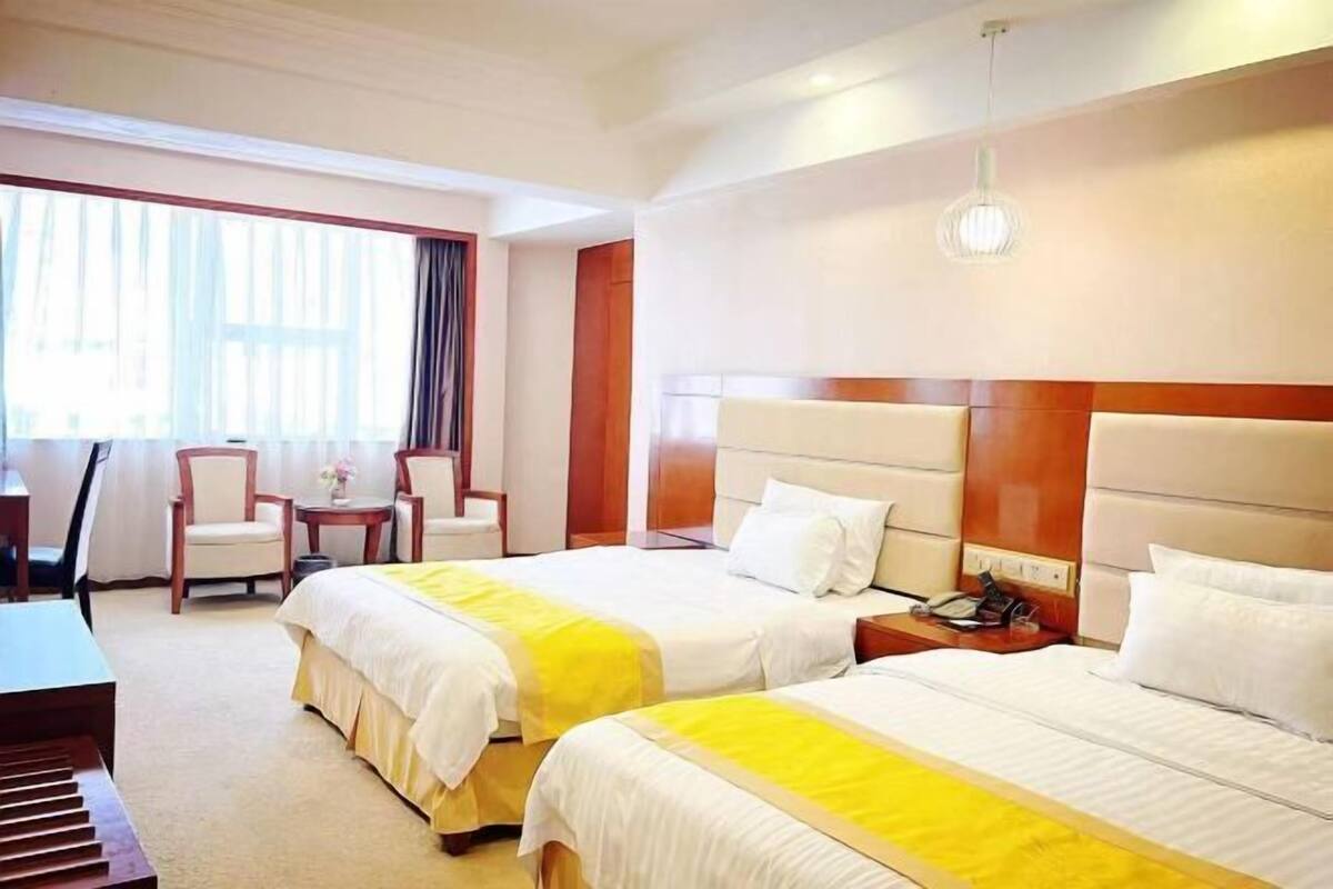 Habitación de hotel con dos camas, un escritorio, sillas y un amplio ventanal con cortinas.