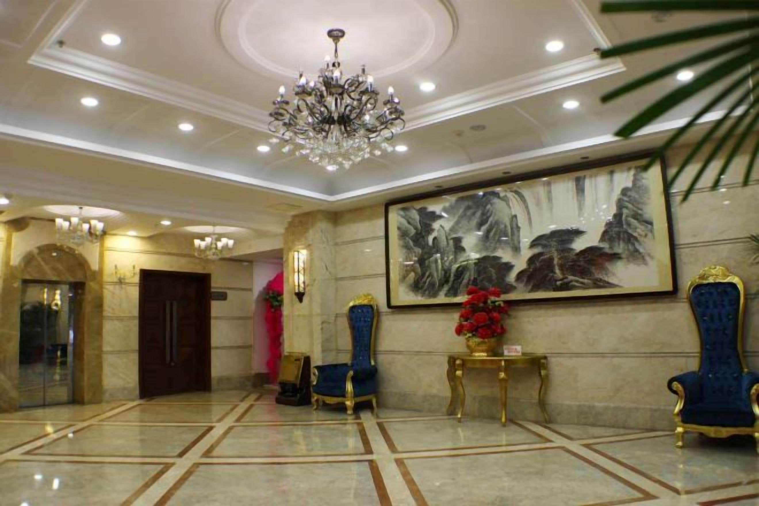 A lobby with a chandelier, a large painting, and two blue armchairs.