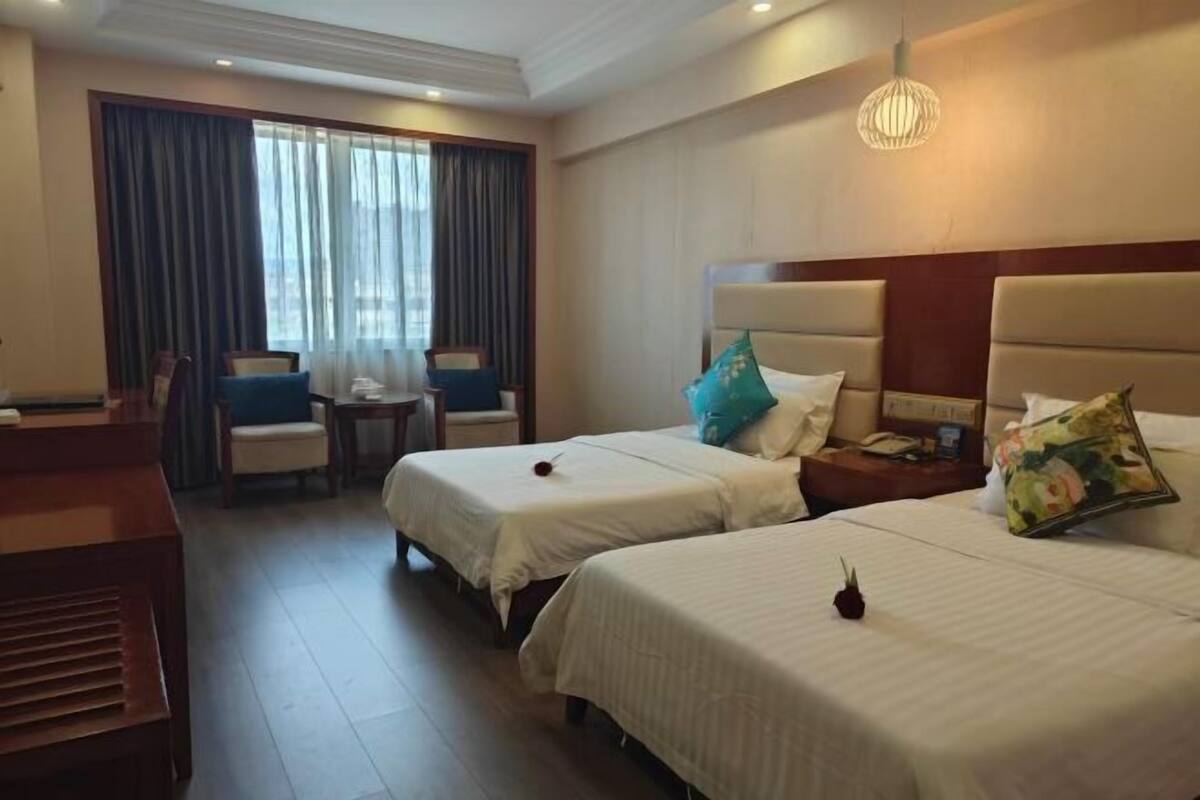 Habitación de hotel con dos camas, un escritorio, una silla, una mesita y una ventana con cortinas.