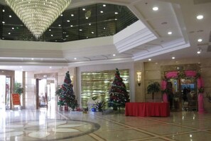 Un hall d’entrée spacieux avec un plafond haut, de grands lustres et des sapins de Noël.