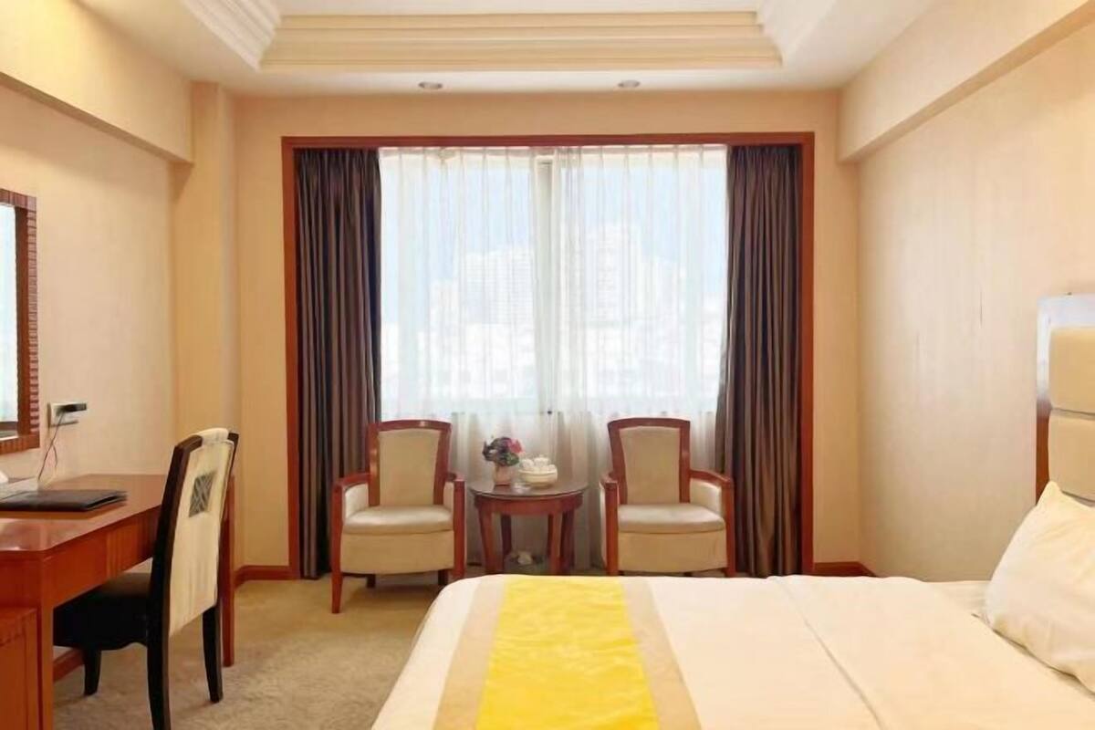 Una habitación de hotel con cama, dos sillas, una mesita y una ventana con cortinas.