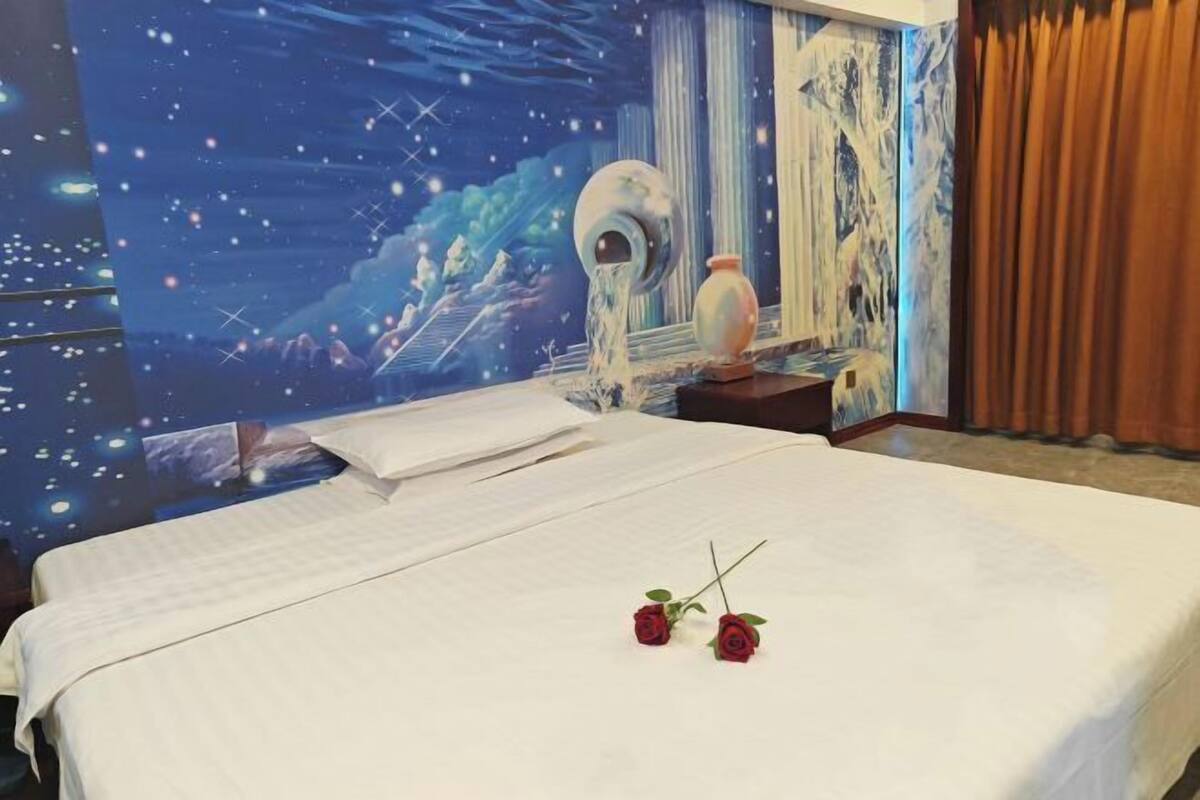 Una habitación de hotel con una cama grande, un mural de cielo nocturno en la pared y un florero en la mesita de noche.