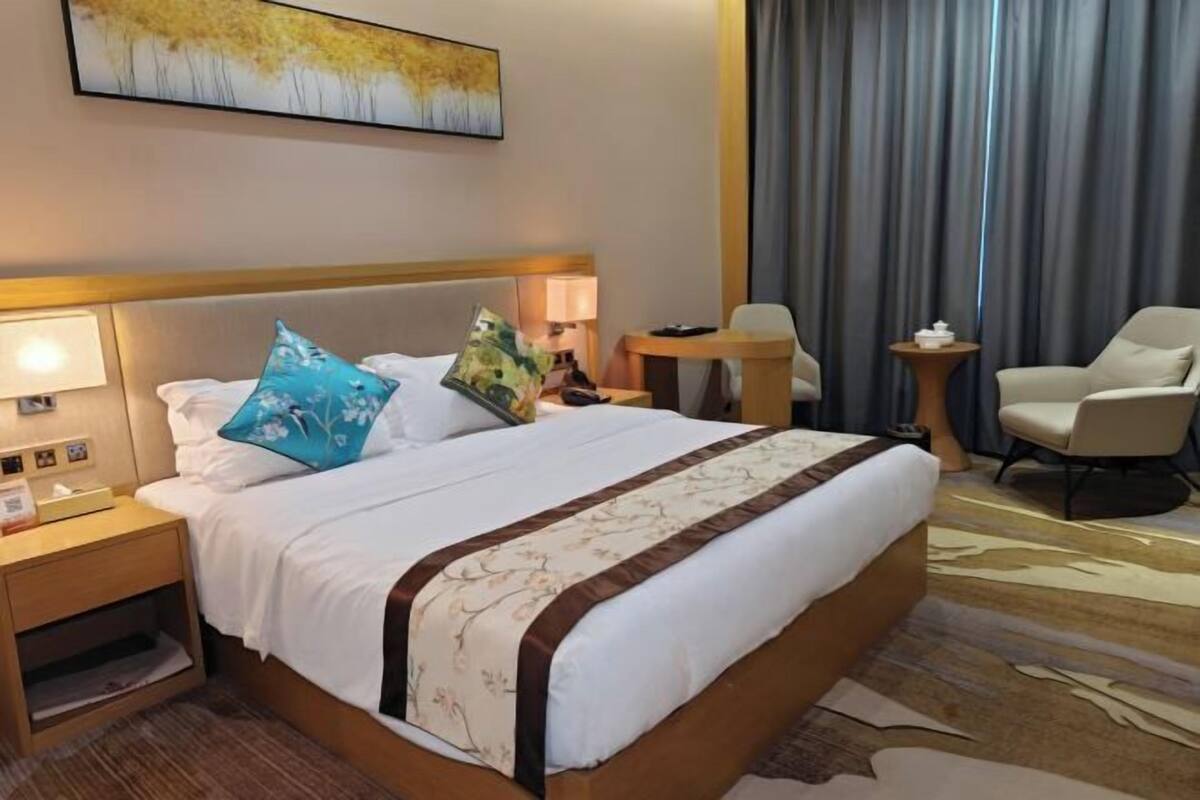 Una habitación de hotel con cama, mesitas de noche, una silla, una lámpara y un cuadro en la pared.