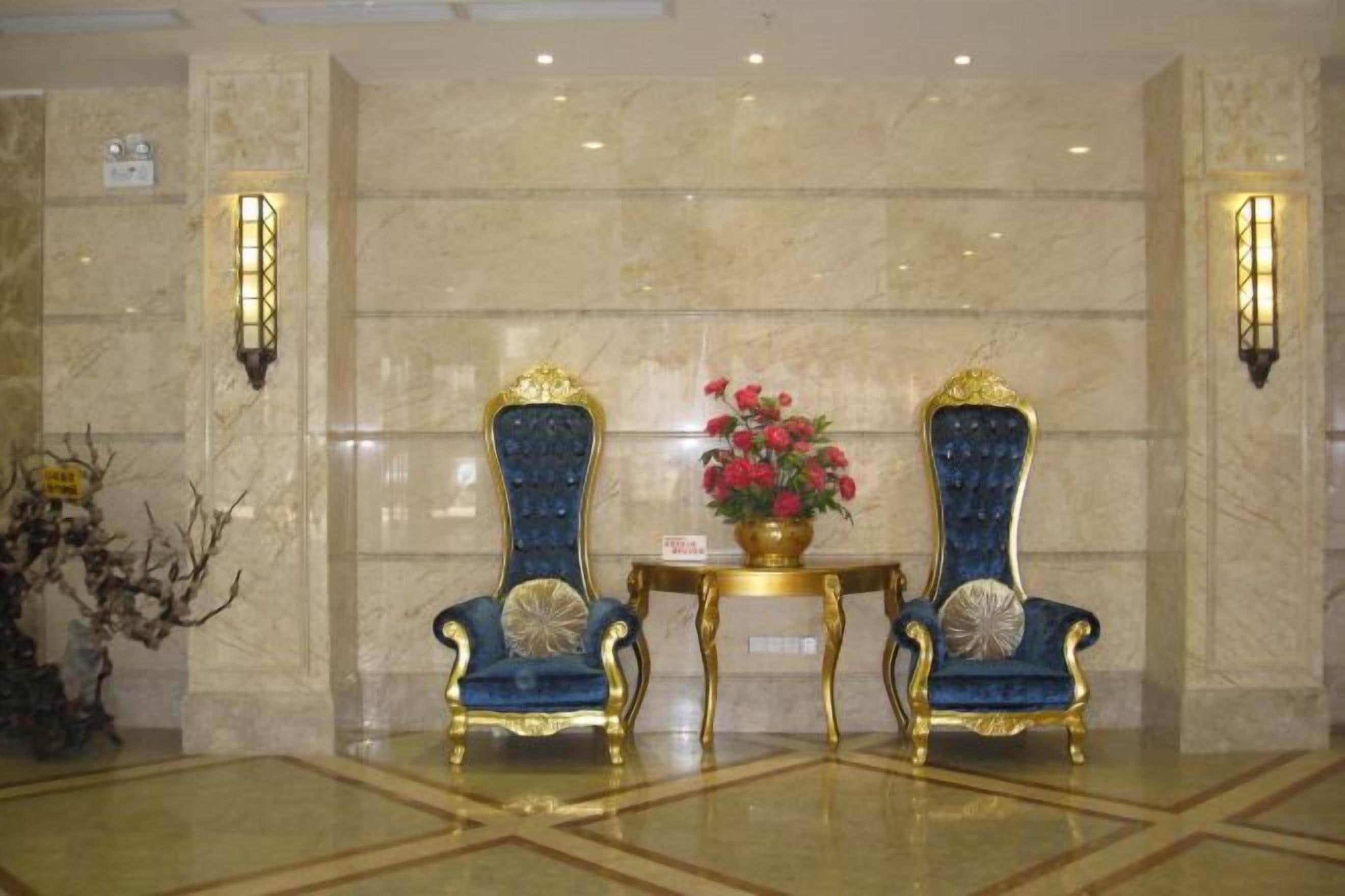 A lobby with two ornate blue and gold chairs, a small table with a vase of flowers, and wall sconces.
