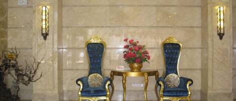 A lobby with two ornate blue and gold chairs, a small table with a vase of flowers, and wall sconces.