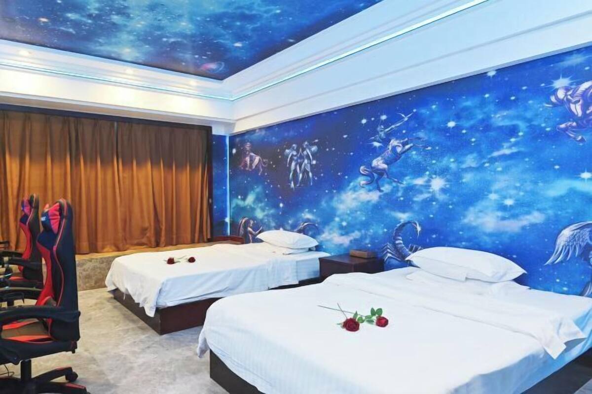Habitación de hotel con dos camas, un mural de estrellas en la pared y una silla gamer.