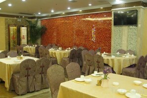 Un salón de banquetes con mesas redondas, sillas y un fondo de pared floral.