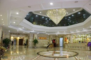 Un vestíbulo de hotel con una imponente araña, una recepción y un suelo de mármol circular.