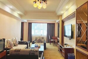 A hotel room with a sofa, a TV, a dining table, and a large window with curtains. - Zhuji Hotel Nanxiong (Nanxiong)