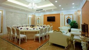Un comedor formal con una mesa redonda, sillas blancas tapizadas, una araña y un televisor en la pared.