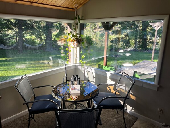 A sunlit patio with a round table and four chairs, overlooking a lush garden and a wooden deck.