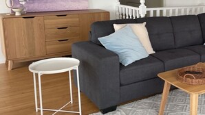 Ein Wohnzimmer mit einem dunkelgrauen Sofa, einem weißen Beistelltisch, einer Holzkommode und einem gemusterten Teppich.