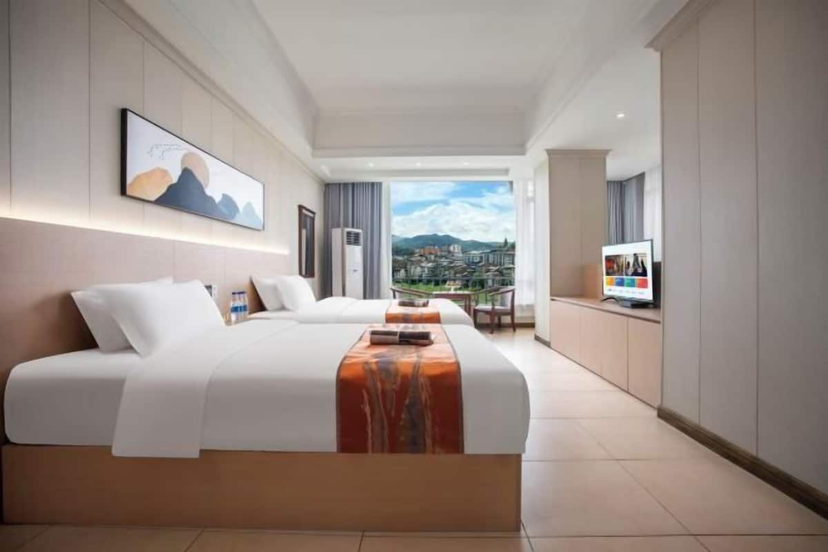 A modern hotel room with a large bed, a TV, and a city view.