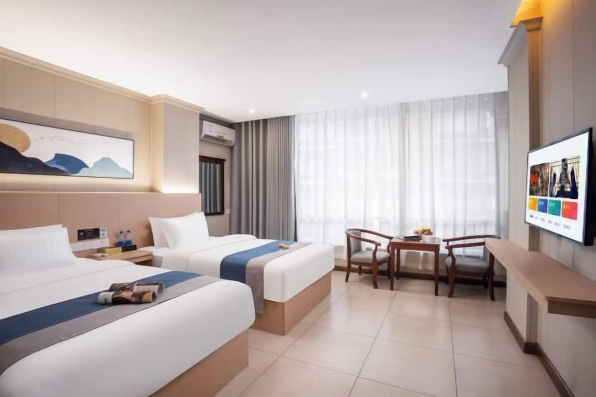 A hotel room with two beds, a desk, a chair, a TV, and a window with curtains.