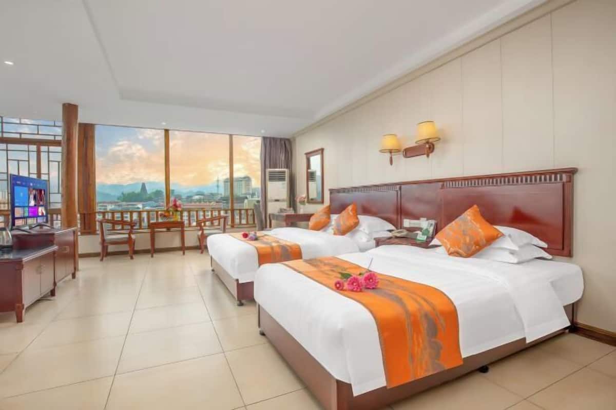 A hotel room with two beds, a desk, and a large window with a city view.