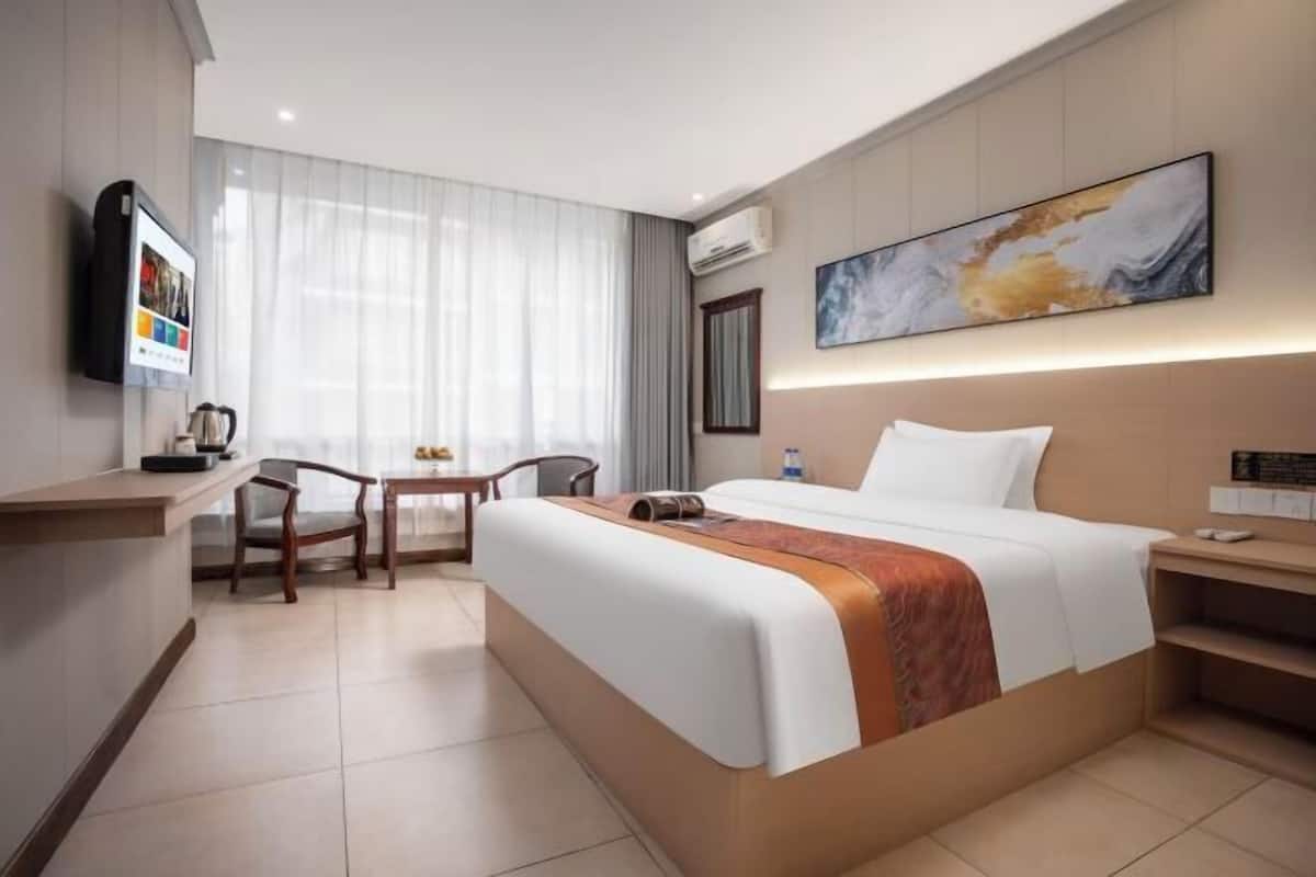 A hotel room with a bed, a desk, a chair, a TV, and a painting on the wall.