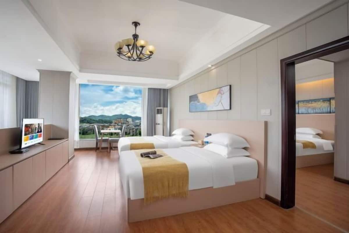 A hotel room with two beds, a TV, a large window with a view, and a chandelier.