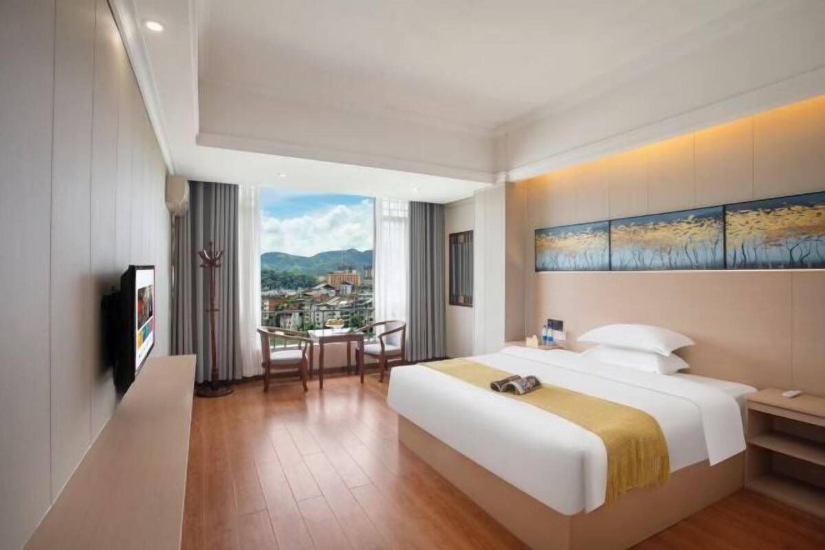 A hotel room with a bed, a desk, a chair, a TV, and a painting on the wall.