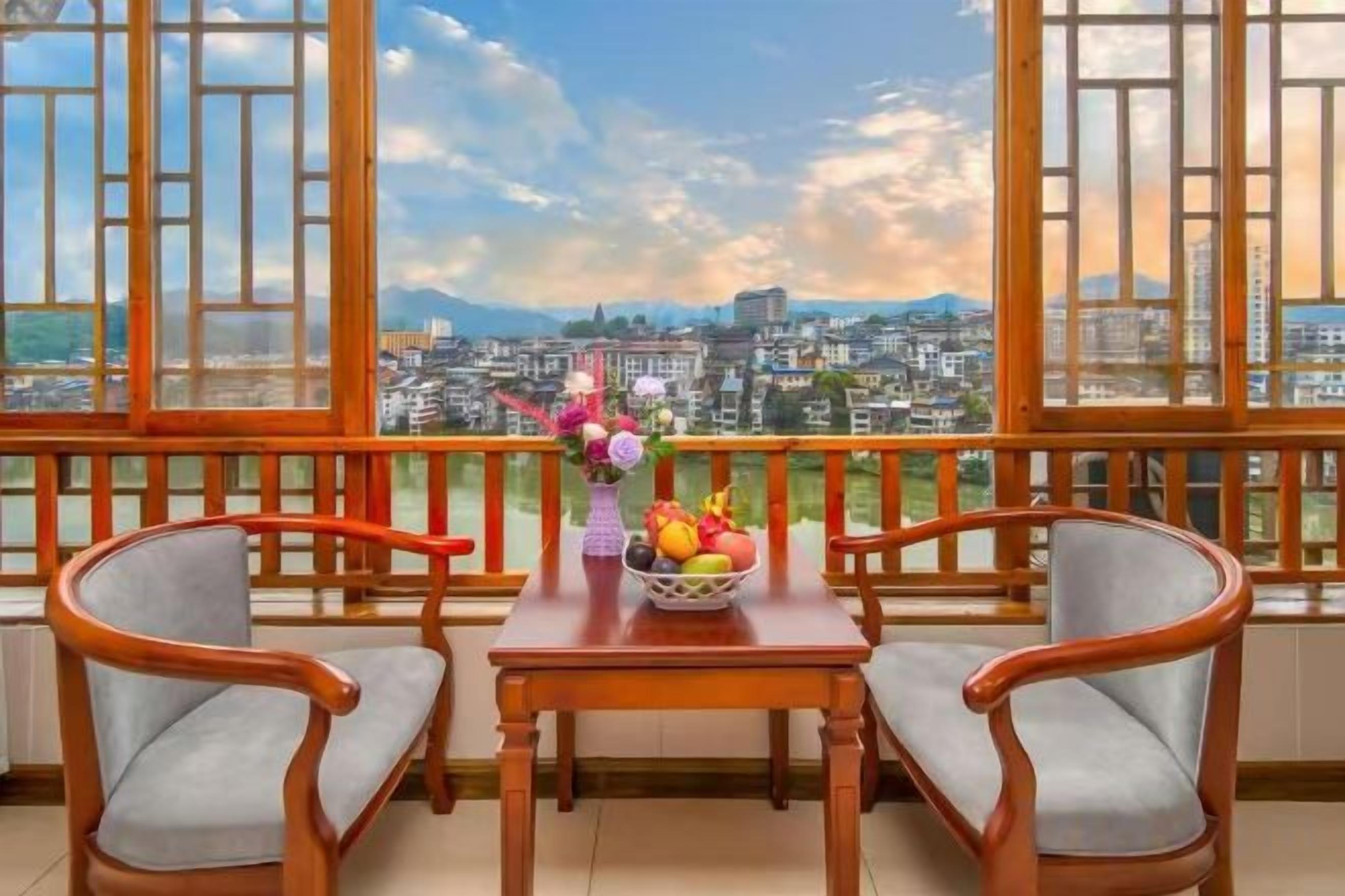 A balcony with a table and two chairs, a vase with flowers, and a bowl of fruit.
