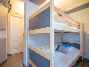 Ein Stockbett mit Holzrahmen und Matratze, eine weiße Tür und ein Lichtschalter an der Wand.