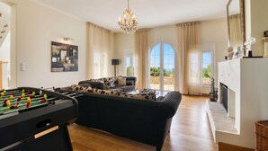 Een ruime woonkamer met een tafelvoetbalspel, een bank, een kroonluchter en een open haard.