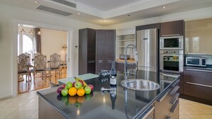 Een moderne keuken met roestvrijstalen apparatuur, een centraal eiland met fruit, en een eetgedeelte met rieten stoelen.
