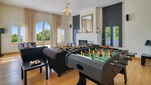 Een kamer met een tafelvoetbaltafel, een bank, een kroonluchter en grote ramen.