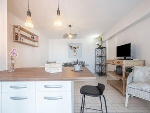 A modern kitchen with a central island, white cabinetry, and a dining area with a wooden table and chairs. - Hacienda 3 by Interhome (Canet-Plage)