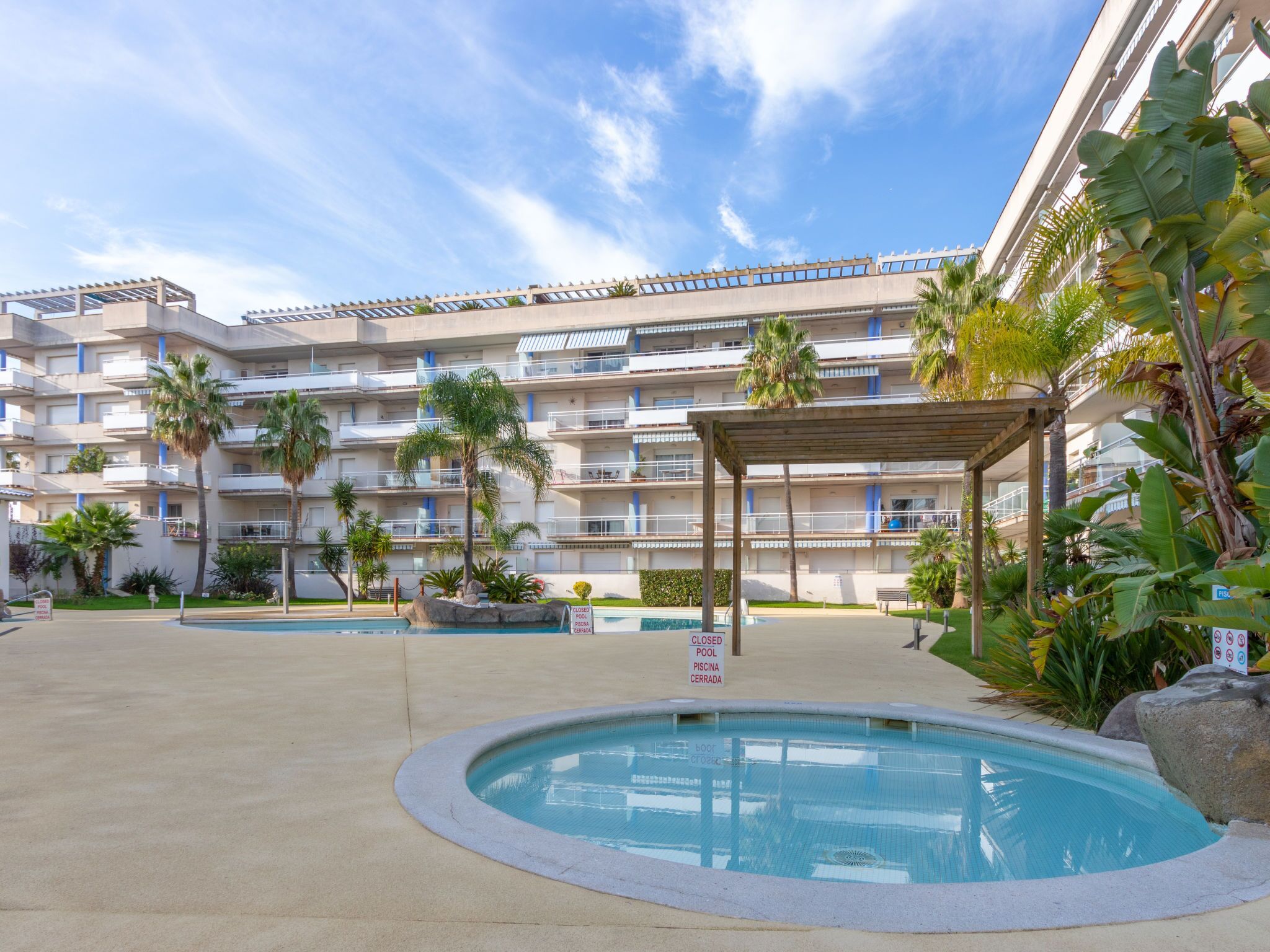 A hotel with a swimming pool, palm trees, and a covered area.