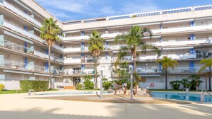 A multi-story hotel with balconies, a swimming pool, and palm trees. - Port Canigó by Interhome (Roses)